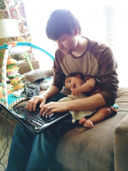 Adoptive father working while getting a hug from his daughter.