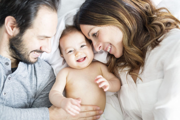 Mother father and baby child on a white bed.